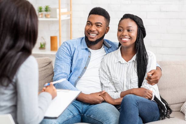 Smiling Black couple holding hands on a couch during a session with a professional counselor.